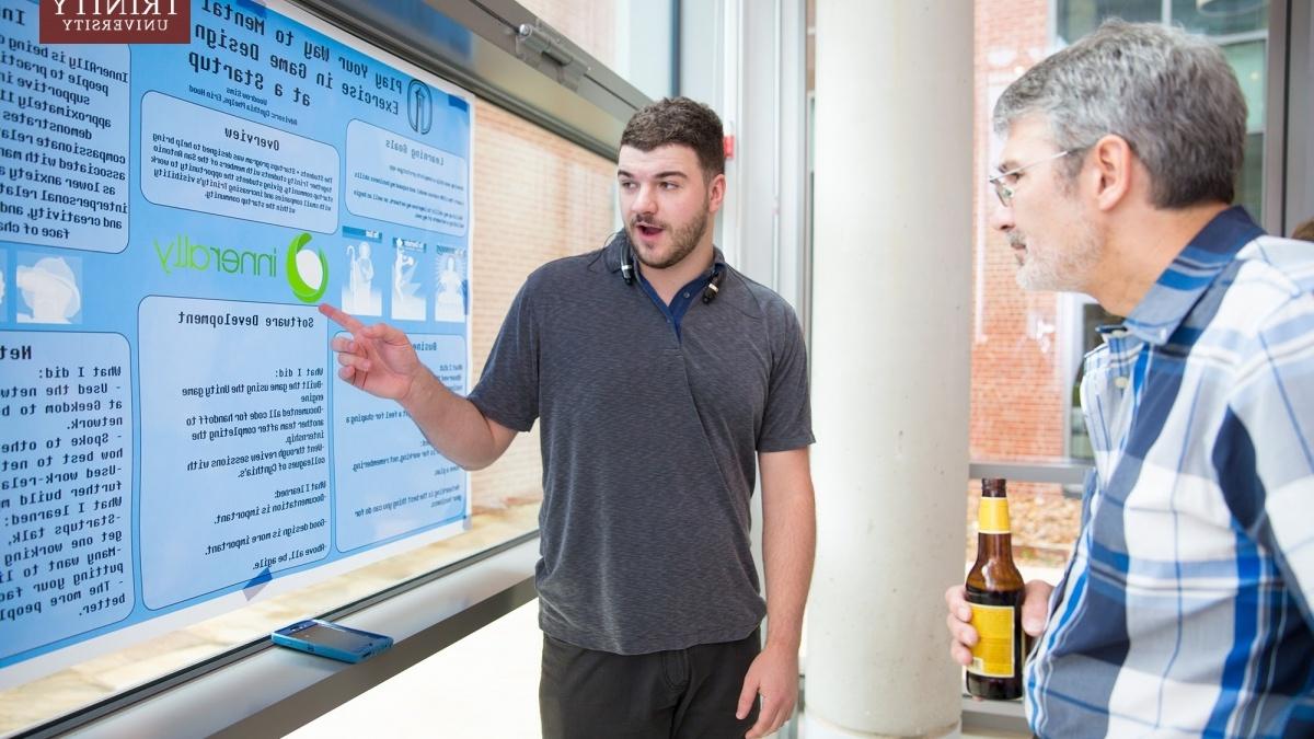 A student points toward code for a game while an onlooker observes. 