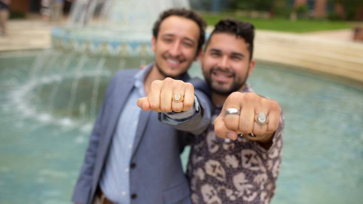 two students show off their class rings next to miller fountain